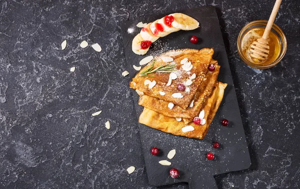 Traditional crepes with banana and berries on black stone background. Copy space