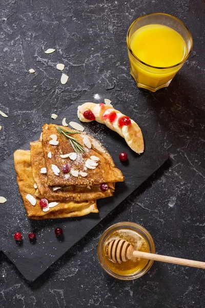 Traditional crepes with banana and berries on black stone background