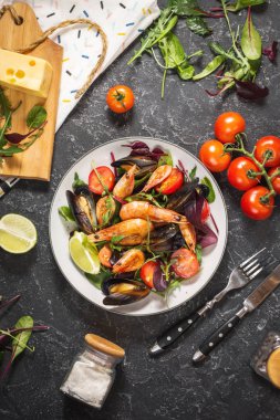 Taze deniz ürünleri salatası, midye, karides, taze sebze ve otlar siyah taş zemin üzerine. Üstten Görünüm