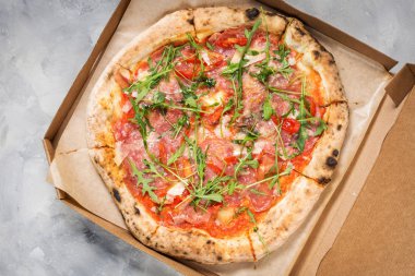 Karton kutu jambon, roka ve parmesan ile lezzetli Pizza ile beton zemin üzerine.