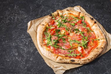 Jambon, roka ve parmesan pizza siyah taş zemin üzerine. Geleneksel İtalyan yemekleri.