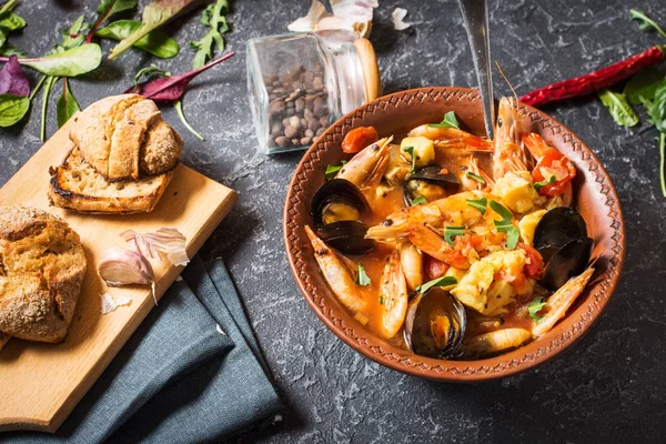 Fransızca balık çorbası Bouillabaisse deniz ürünleri, somon fileto, karides, midye siyah taş zemin üzerine. Lezzetli akşam yemeği