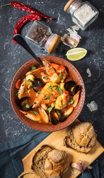 French fish soup Bouillabaisse with seafood, salmon fillet, shrimp, mussels on black stone background. Delicious dinner. Top view — Stock Image French Fish Soup Bouillabaisse Seafood Salmon Fillet Shrimp Mussels Black Royalty Free Stock Images