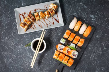 Siyah taş arka planda servis edilen suşi ruloçeşitleri.