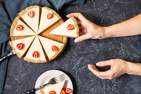 Kadın el siyah taş arka plan üzerinde taze çilek ile Ev yapımı cheesecake bir dilim tutun