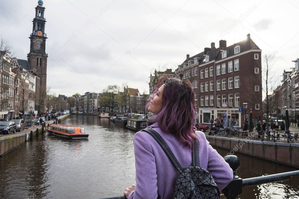 Girl in the coat and backpack enjoying Amsterdam city. Young woman looking to the side on Amsterdam channel