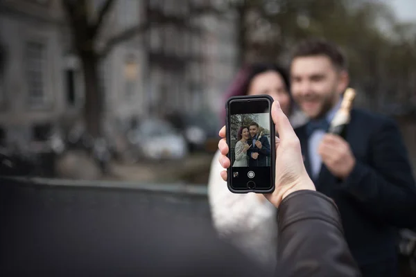 Somebody is using smartphone to make a photo of newlyweds in the city