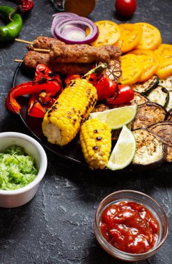 Koyu taş arka planda çeşitli lezzetli ızgara sebzeler ve et. Yaz yemekleri