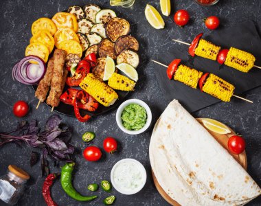 Koyu taş arka planda çeşitli lezzetli ızgara sebzeler ve et. Yaz yemekleri Barbekü.