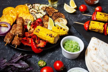 Koyu taş arka planda çeşitli lezzetli ızgara sebzeler ve et. Yaz yemekleri