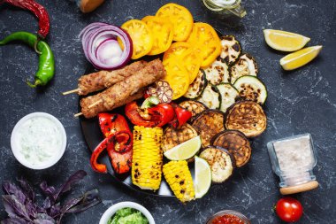Koyu taş arka planda çeşitli lezzetli ızgara sebzeler ve et. Yaz yemekleri