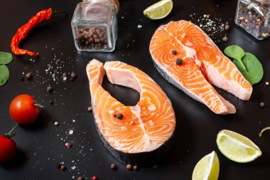 İki taze çiğ somon bifteği, tuz, biber ve siyah arka planda limon..