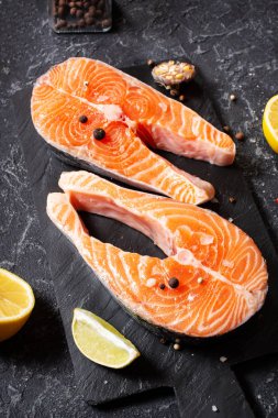 İki taze çiğ somon bifteği, tuz, biber ve arkaplanda limon..
