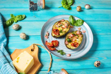 Keto diyeti: jambonlu avokado, bıldırcın yumurtası, mavi ahşap arka planda peynir.