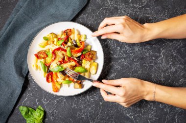 Kadın elleri çatal ve bıçak tutuyor. Izgara sebzeli makarna - kabak, patlıcan, biberli domates