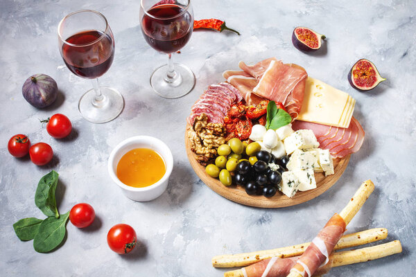 Italian antipasto with prosciutto, ham, cheese, olives and grissini breadsticks on concrete background. Top view
