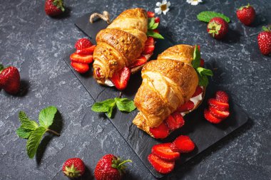 Lezzetli bir kahvaltı. Siyah taşlı arka planda taze kruvasan ve çilek.