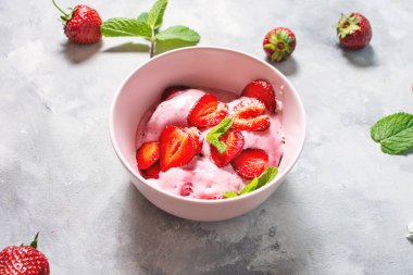 Çilekli dondurma pembe bir kasede, arka planda çilekler var.