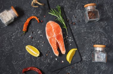 Siyah taş zemin üzerinde tuz, biber, limon ve biberiye ile taze çiğ somon bifteği.