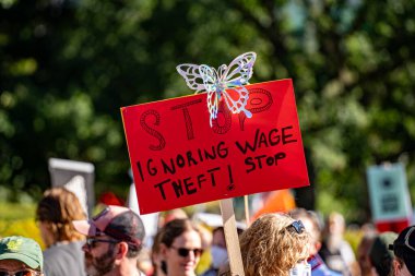 Protesto yazısı diyor ki, maaş hırsızlığını kelebek süslemesiyle görmezden gelmeyi bırak. Toronto, Kanada - 20 Eylül 2025.