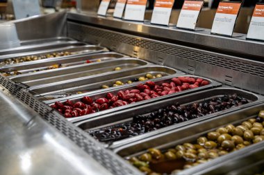 Close up of assorted olives displayed in stainless steel salad bar containers.