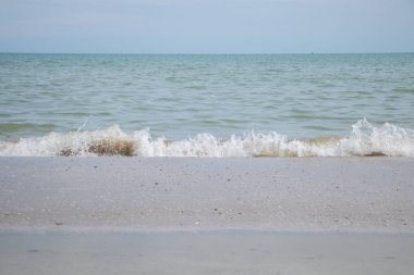 Küçük deniz dalgaları kumlu sahilde mavi ufuk ve sakin okyanus suyuyla yaz tatili boyunca kırılıyor..