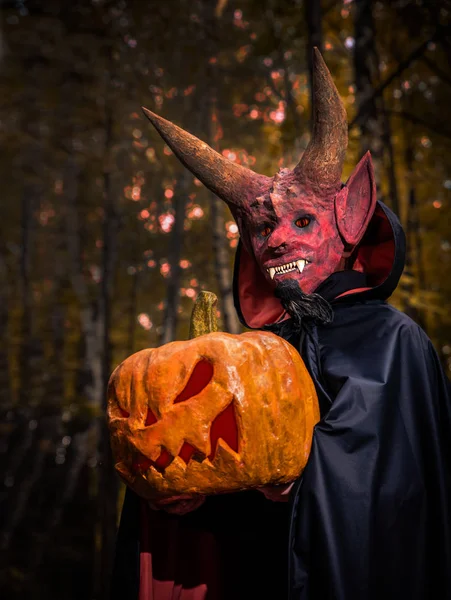 Диявол з гарбузом в руках на Хелловін у темному лісі — стокове фото