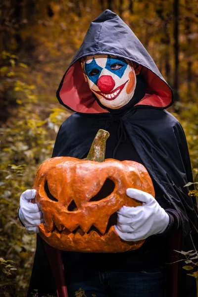 Muž v klaunské masce s dýní v dlaních pro Hallowee — Stock fotografie
