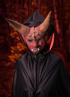 Devil with horns and in a black cloak on a red background clipart