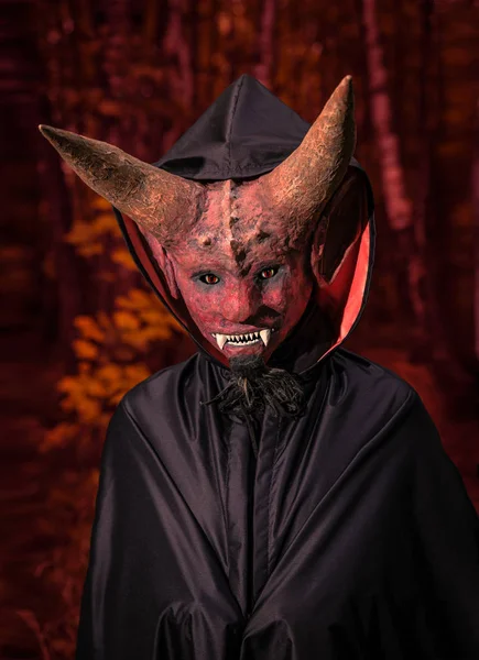 Дьявол с рогами и в черном плаще на красном фоне — стоковое фото