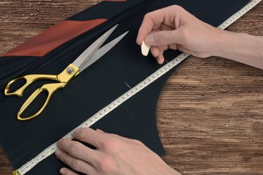 Terzi kumaşın üzerindeki bir mezura ile kesiği işaretliyor. Adam ahşap bir masada çalışıyor.