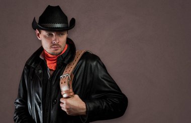 Şapkalı ve pelerinli traşsız bir adam. Elinde kemer olan deri elbiseli bir kovboy. Duvarın arkasında maço bir adam var. Batı Amerika kültür kavramı