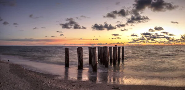 Dilapidated ruins of a pier on Port Royal Beach at sunset in Naples, Florida