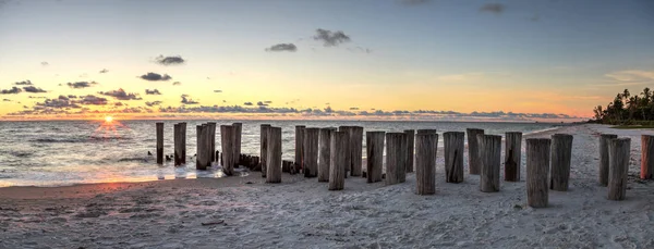 Dilapidated ruins of a pier on Port Royal Beach at sunset in Naples, Florida