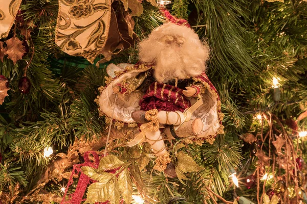 Santa Clause ornament on a Christmas tree with white lights and bows and festive decorations around the holiday season.