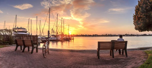 Fahrrad und Mann sitzen bei Sonnenaufgang auf einer Bank über der Stadt. — Stockfoto