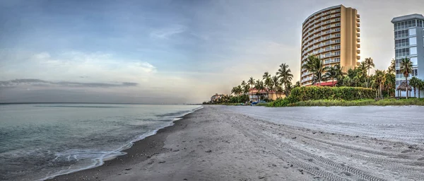 Vanderbilt Beach at sunrise with a calm ocean and buildings along the white sand in Naples, Florida.