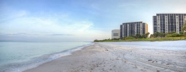 Güneşin doğuşuyla birlikte sakin bir okyanus ve Napoli, Florida 'daki beyaz kumlar boyunca binalar..
