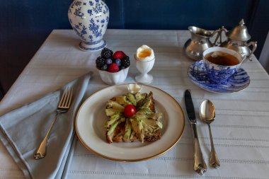 Avokado tostu, karışık böğürtlen, çay ve kahvaltıda mavi vazolu bir masada kaynamış yumurta..