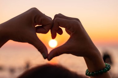 Gün batımında aşk dolu kalp şeklinde Siluet Eller. Kalbin kadın eli gökyüzüne karşı. Güneş ışınları, aşkta mutluluk.