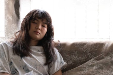 Kanepede oturan Asyalı genç kız dalgın, yalnız kız konsepti olmalı.