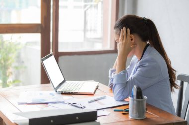 Asyalı iş kadınları baş ağrısı ve stres hissediyorlar. O, dizüstü bilgisayarın önündeki ofis masasında çalışıyor. İş ve finans kavramı.