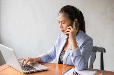 Ofiste bilgisayarla çalışan Asyalı iş kadını telefonla konuşurken bilgisayardan bilgi alıyor..