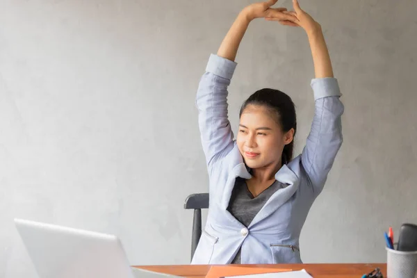 Business women or working lady are stretch oneself or lazily for relaxation on her desk while doing her work in the office.
