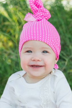 Gülümseyen çocuk çim pembe şapkalı. Şapka polka noktaları. Yeşil çim. Gülümseyen çocuk.