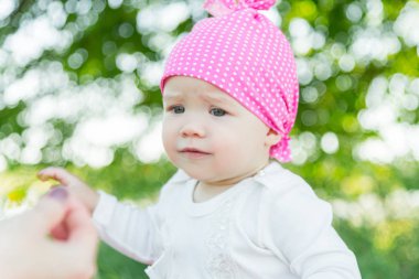 Gülümseyen çocuk çim pembe şapkalı. Şapka polka noktaları. Yeşil çim. Gülen çocuk. Çocuk bir çiçek alır.