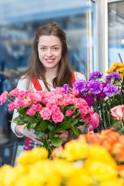 flower seller, young woman standing at shop with  flower in hands happily looks at camera