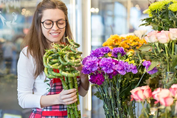 flower seller, young woman standing at shop with  flower in hands happily looks at camera