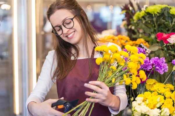 flower seller, young woman standing at shop with  flower in hands happily looks at camera