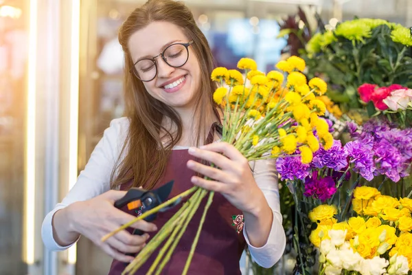 flower seller, young woman standing at shop with  flower in hands happily looks at camera